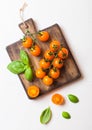 Organic Cherry Orange Rapture Tomatoes on the Vine with basil on chopping board on white kitchen background.