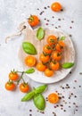 Organic Cherry Orange Rapture Tomatoes on the Vine with basil and pepper on chopping board on stone kitchen background.