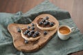 Organic chocolate hazelnut spread with fresh blueberries on ciabatta slices on wood board and fresh espresso in white