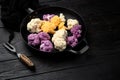 Organic colorful cauliflowers, on frying cast iron pan, on black wooden table background Royalty Free Stock Photo