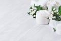 Organic delicate white cosmetics products - cream, salt, clay, scrub and bath cotton towel, flowers on white wooden background.
