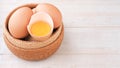 Organic egg half-cracked with yolk in wicker basket on white wooden background. Royalty Free Stock Photo