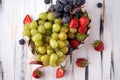 Organic fresh berries of green and blue grapes, strawberries, raspberries, blueberries in a basket on a light wooden background. Royalty Free Stock Photo