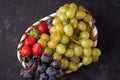 Organic fresh berries of green grapes, strawberries, raspberries, blue blueberries in a basket on a dark concrete background. Royalty Free Stock Photo