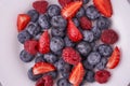 Organic fresh berries of strawberry, raspberry, blackberry, blueberry on a white plate on a light wooden background.