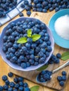 Organic fresh blueberries in bowl with mint leaves and sugar on a wooden table.