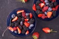 Organic fresh ripe blackberries, strawberries, raspberries, blueberries in blue saucers on a dark concrete background. Royalty Free Stock Photo