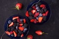 Organic fresh ripe blackberries, strawberries, raspberries, blueberries in blue saucers on a dark concrete background. Royalty Free Stock Photo