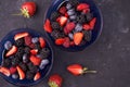 Organic fresh ripe blackberries, strawberries, raspberries, blueberries in blue saucers on a dark concrete background. Royalty Free Stock Photo