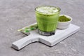 Organic green matcha tea latte in glass and powder in white bowl on white wooden board Royalty Free Stock Photo