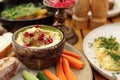 Organic humus in a bowl, decorated with pomegranate seeds, served with vegetable snacks, on a plate, on a wooden table.