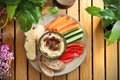 Organic humus in a bowl, decorated with pomegranate seeds, served with vegetable snacks, on a plate, top view.