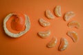 Organic mandarin wedges arranged in a circle with the peel next to them in a spiral on an orange paper background