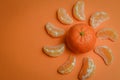 Organic mandarin wedges arranged in a circle with a whole mandarin in the center on an orange paper background with space for text