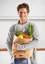 Only organic for me. A young man in a kitchen holding a brown paper bag filled with vegetables. Royalty Free Stock Photo