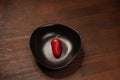 Organic mini red bell pepper laying lonely in a deep black bawl and ready to eat isolated on wooden background Royalty Free Stock Photo