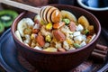 Organic oatmeal porridge with bananas, honey, almonds, pistachio, coconut, kiwi fruit, cinnamon, raisins in dark ceramic bowl