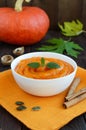 Organic pumpkin puree soup in a white bowl on dark wooden background. Royalty Free Stock Photo