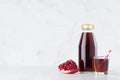 Organic red garnet juice juice in glass bottle mock up with straw, wine glass, fruit slice on white wood table in light interior.