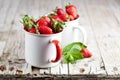 Organic red strawberries in two white ceramic cups and mint leaves on rustic wooden background Royalty Free Stock Photo