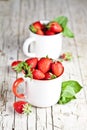 Organic red strawberries in two white ceramic cups and mint leaves on rustic wooden background Royalty Free Stock Photo