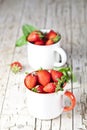 Organic red strawberries in two white ceramic cups and mint leaves on rustic wooden background Royalty Free Stock Photo