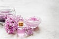 Organic salt, cream, extract in lilac cosmetic set with flowers on stone table background