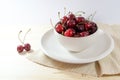 Organic sweet cherries in an off-white ceramic bowl and plate with a napkin on a light wooden table, fresh fruits as summer snack Royalty Free Stock Photo