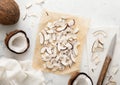 Organic sweet coconut slices chips on in baking tray with knife and ripe coconuts on light table Royalty Free Stock Photo