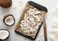 Organic sweet coconut slices chips on in baking tray with knife and ripe coconuts on light table.Top view Royalty Free Stock Photo