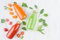 Organic tomato, carrot, spinach juices in glass bottles with ingredients, green leaves on white wood board, mock up for design.