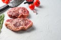 Organic top blade steak, raw beef meat with seasonings, rosemary and butcher cleaver. White textured background. Side view with Royalty Free Stock Photo