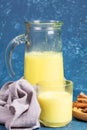 Organic turmeric milk. Decanter and glass with golden milk, napkin and ingredients on blue background.