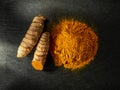 Organic turmeric powder and fresh curcuma roots on a black slate surface. Raw and ground rhizomes of curcuma longa. Concepts of Royalty Free Stock Photo