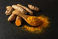 Organic turmeric powder in a wooden spoon and raw curcuma roots on a black slate background. Fresh and ground rhizomes of curcuma Royalty Free Stock Photo