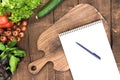 Organic vegetables, chopping board and blank notepad with pen on wooden background Royalty Free Stock Photo