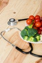 Organic vegetables on plate near stethoscope on wooden surface