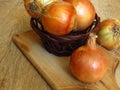 Organic yellow onions in a basket rustic style setting on a chopping board and oak tree wood background.