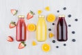 Organic yellow orange, pink strawberry and violet blueberry juices in glass bottles with fruit ingredients on white wood board