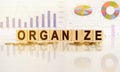 ORGANIZE the word on wooden cubes, cubes stand on a reflective surface, in the background is a business diagram