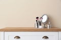 Organizer with makeup cosmetic products and mirror on table against light wall