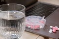 Organizer weekly shots with glass of water on workplace background and laptop Closeup of medical pill box with doses of