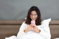 Oriental lady happily playing with mobile phone in bedroom