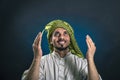 Oriental-looking man in traditional Arab national dress smiles happily, raising his eyes and hands to heaven