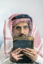 Oriental man in white, traditional, national, Arabic dress dishdash, thoughtfully holding an old large book in his hands