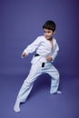 Oriental martial arts. Aikido fighter, Caucasian 10 years old boy in kimono improves his fighting skills, isolated on violet