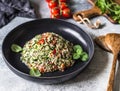 Oriental tabbouleh salad with couscous, vegetables and herbs in a black bowl on a gray background