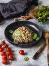 Oriental tabbouleh salad with couscous, vegetables and herbs in a black bowl on a gray background