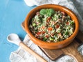 Oriental tabbouleh salad with couscous, vegetables and herbs in a brown ceramic bowl on a blue wood background