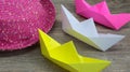 Origami, colorful boats and pink hat on wooden background, hobby